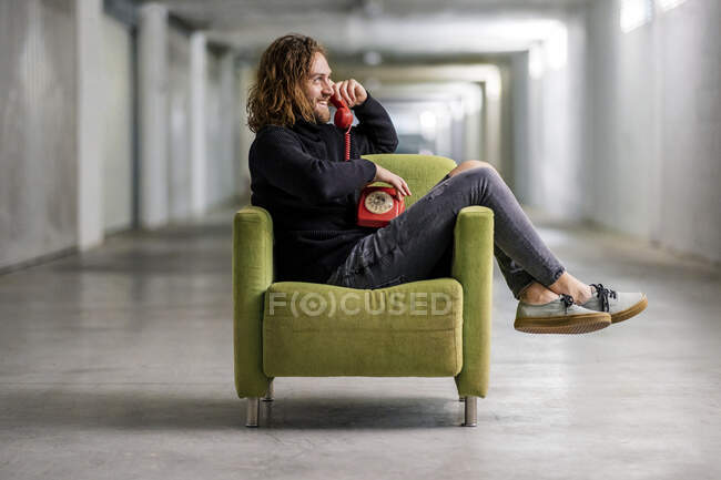 Sonriente hombre hablando por teléfono mientras está sentado en el sillón en casa - foto de stock