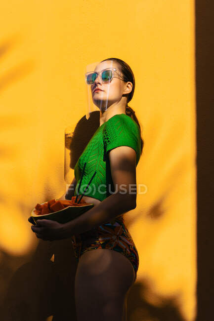 Mujer en colorido patio trasero, con gafas de sol uner protector facial - foto de stock