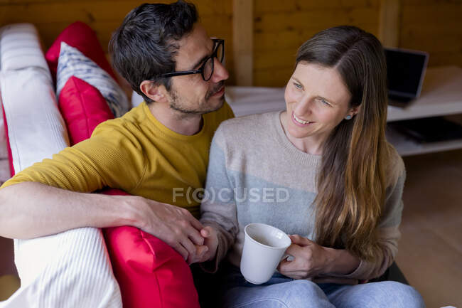 Homem olhando para a namorada pensativa segurando café enquanto sentado no sofá na cabine de log — Fotografia de Stock