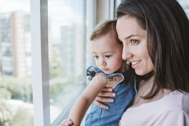 Мама с маленькой девочкой дома, смотрит в окно — стоковое фото