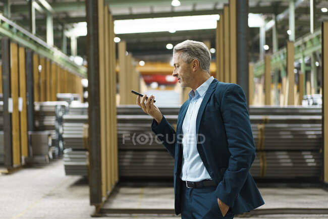 Зрелый бизнесмен держит мобильный телефон на заводе — стоковое фото