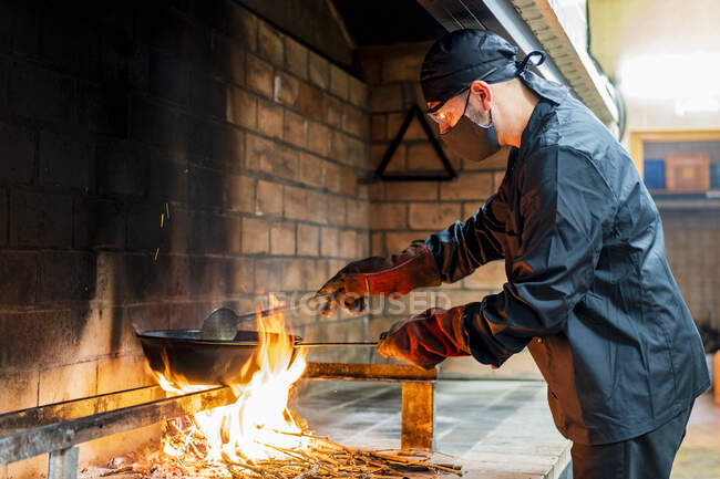 Cozinha tradicional de paella na cozinha do restaurante, chef vestindo máscara protetora — Fotografia de Stock