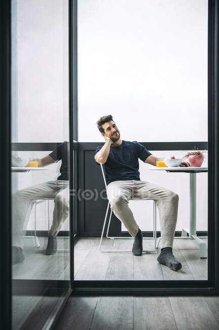 Homme réfléchi souriant assis sur une chaise au balcon dans un penthouse — Photo de stock