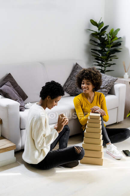 Dos mujeres jóvenes sentadas en el suelo en casa apilando cajas en la sala de estar - foto de stock