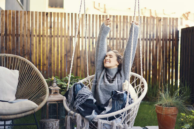 Happy young woman with arms raised relaxing on swing in yard — Stock Photo