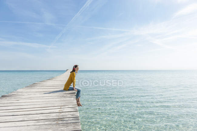 Woman sitting on jetty listening music with headphones, Mallorca, Spain — Stock Photo