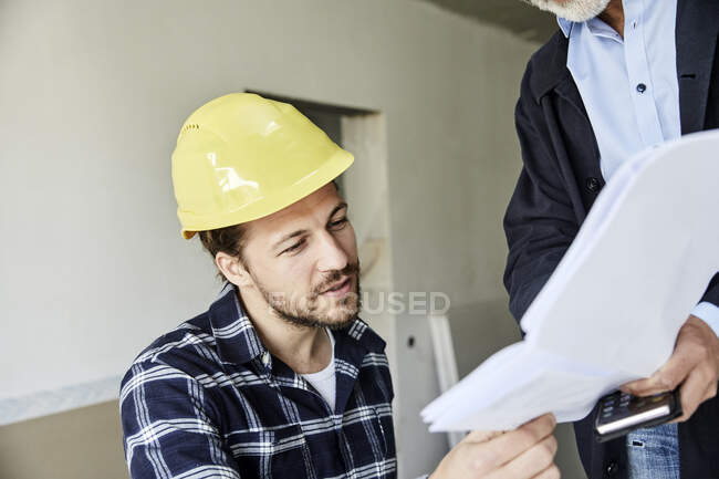 Architect and worker discussing building plan on a construction site — Stock Photo