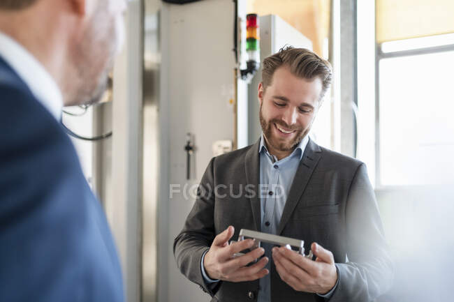Smiling young businessman in a factory holding workpiece — Stock Photo