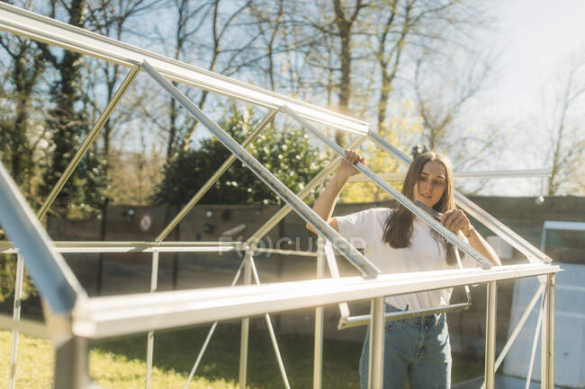 Giovane donna che costruisce serra in cortile durante la giornata di sole — Foto stock