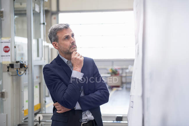 Homme d'affaires mature regardant une planche dans une usine — Photo de stock
