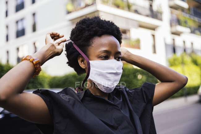 Retrato de una mujer joven que se pone una máscara protectora al aire libre - foto de stock