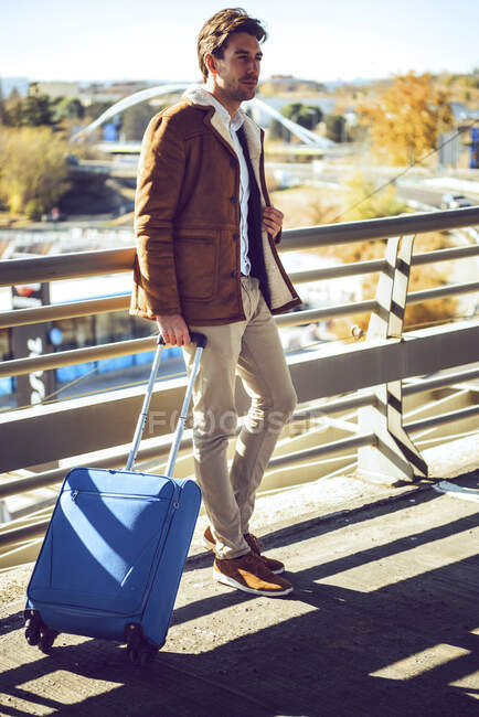 Pensativo hombre de negocios sosteniendo el equipaje mientras está de pie en la pasarela elevada en el aeropuerto durante el día soleado — Stock Photo
