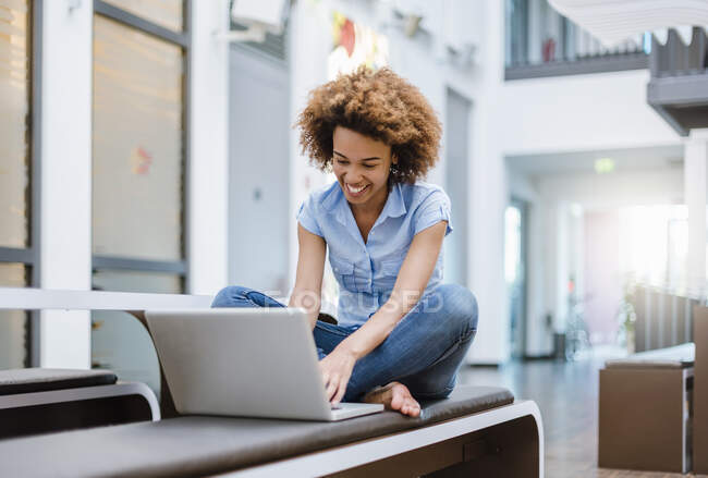 Молода жінка сидить на лавці в сучасному офісі з ноутбуком. — стокове фото