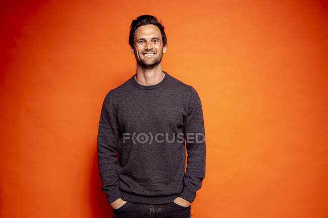 Happy handsome man with hands in pockets against orange background — Stock Photo