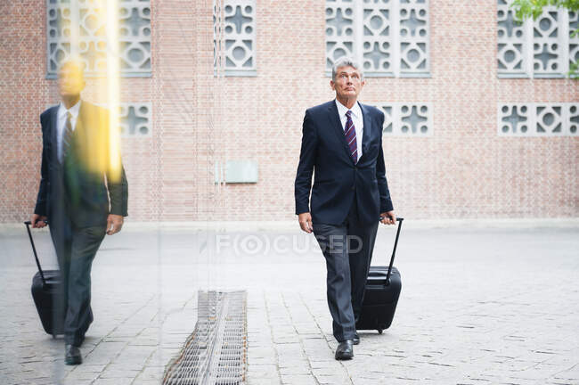 Ritratto di uomo d'affari anziano che tira borsa di carrello su un quadrato — Foto stock