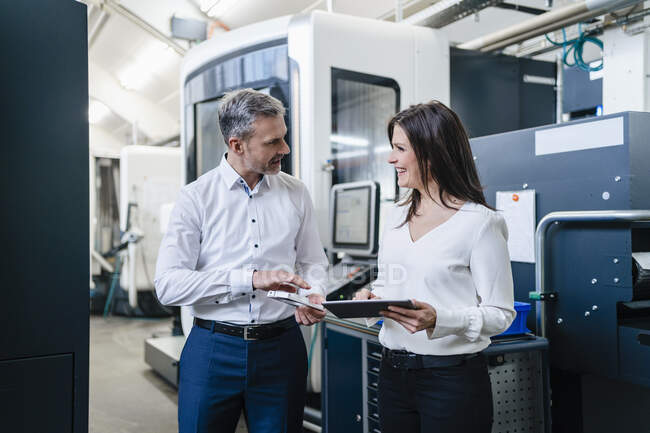 Businessman and businesswoman with product and tablet having a work meeting in a factory — Stock Photo