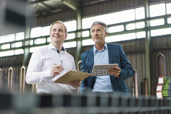 Dois empresários com tablet e prancheta tendo uma reunião em uma fábrica — Fotografia de Stock