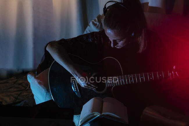Жінка-музикант грає на гітарі на дивані в студії звукозапису вдома — стокове фото