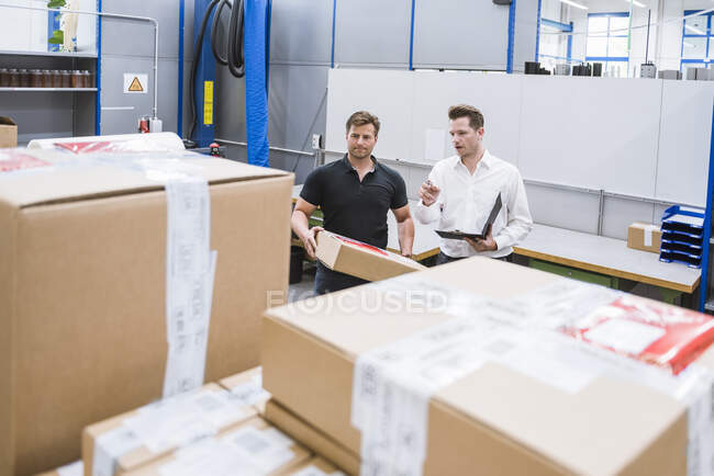 Двое мужчин с посылкой и планшетом на складе завода — стоковое фото