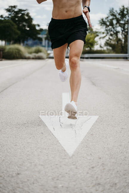 Male athlete running with arrow sign on the road — Stock Photo