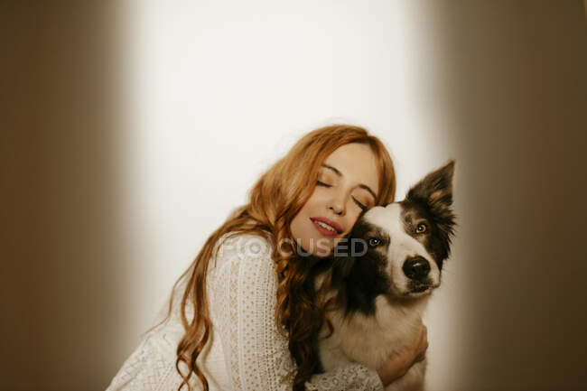 Femme blonde à la maison en pyjama embrassant son chien collie frontière — Photo de stock