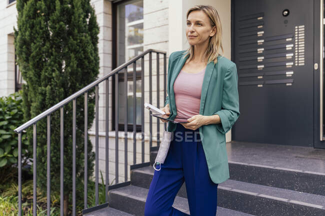 Woman with digital tablet and face mask in hand walking down stairs of house — Stock Photo