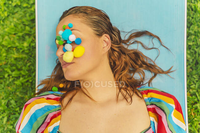 Portrait de femme avec des pompons colorés sur son visage relaxant sur une chaise longue — Photo de stock