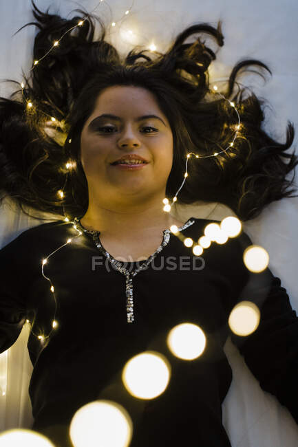 Giovane donna fiduciosa con sindrome di Down sdraiata sul letto illuminato a casa — Foto stock