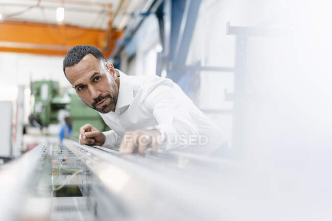 Бизнесмен осматривает металлический стержень в заводском зале — стоковое фото