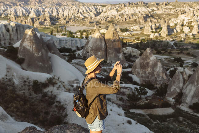 Vista laterale della giovane donna che fotografa formazioni rocciose con smartphone a Goreme, Cappadocia, Turchia — Foto stock