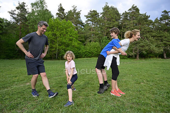 Happy parents exercising with children on grassy land against trees in forest — Stock Photo