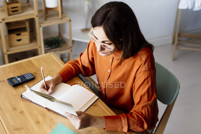 Женщина-фрилансер, работающая дома, сидит за столом с помощью калькулятора — стоковое фото