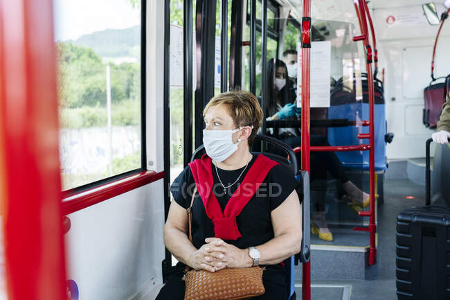 Портрет зрелой женщины в защитной маске в общественном автобусе, выглядывающей в окно, Испания — стоковое фото