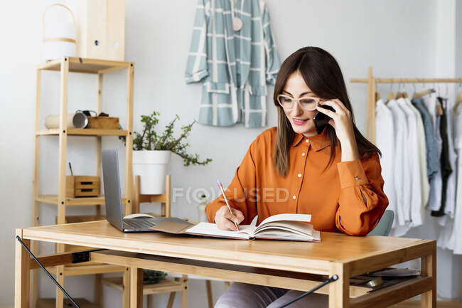 Женщина-дизайнер, работающая дома, сидит за столом и делает заметки. — стоковое фото