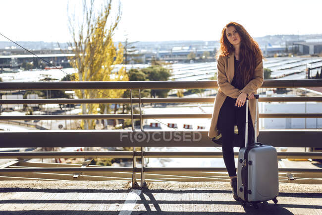 Mujer de negocios confiada sosteniendo equipaje en la pasarela elevada en el aeropuerto durante el día soleado — Stock Photo