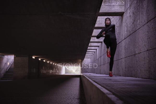 Athlète féminine s'échauffant avant de courir dans un passage souterrain piétonnier — Photo de stock