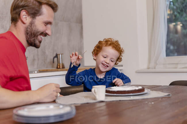 Happy father and son looking at chocolate cake on dining table in kitchen — Stock Photo
