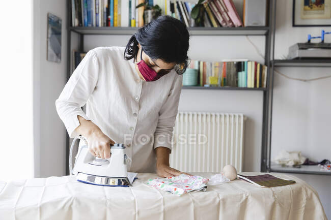 Woman ironing homemade mask on board during pandemic — Stock Photo