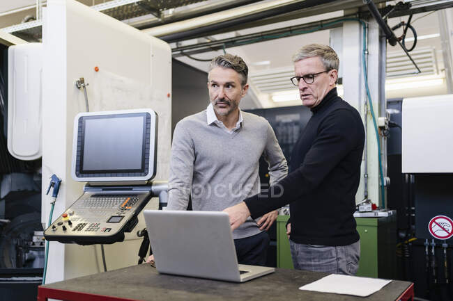 Зрілі чоловіки-наглядачі обговорюють ноутбук на заводі — стокове фото