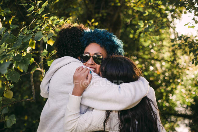 Loving children embracing mother with blue hair against trees in park — Stock Photo