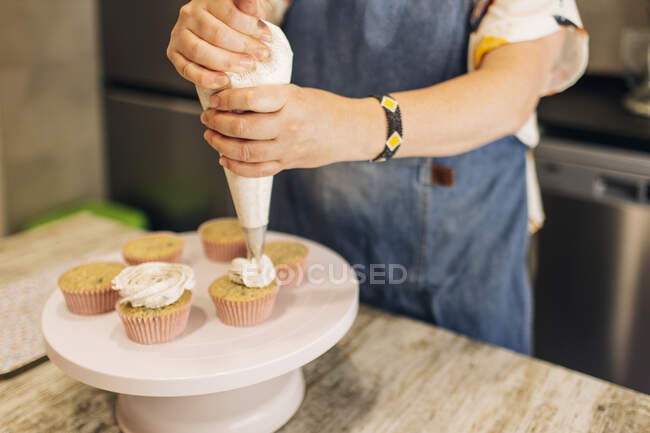 Крупный план зрелой женщины глазурь кексы на торт в мастерской — стоковое фото