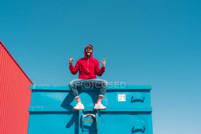 Молодий чоловік у червоній шубці, сидячи на краю синьої тарілки, робить знак рогів — стокове фото