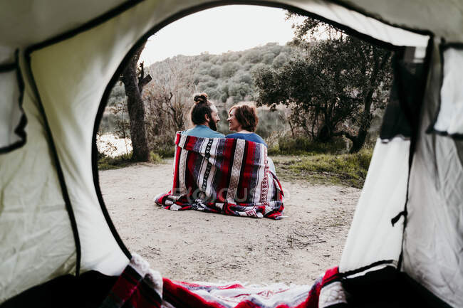 Pareja envuelta en una manta acampando a orillas del lago - foto de stock