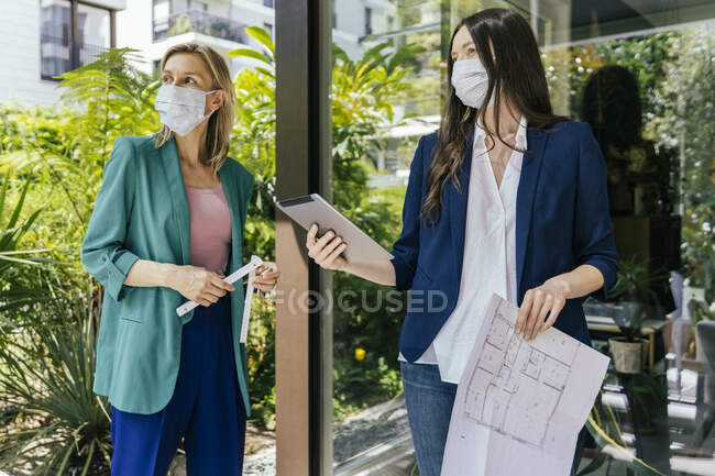 Dos agentes inmobiliarios que usan máscaras faciales mientras inspeccionan el área al aire libre de la casa - foto de stock