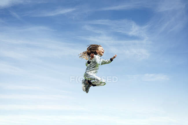 Full length of carefree girl in space suit jumping against blue sky — Stock Photo