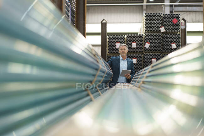 Uomo d'affari maturo che tiene tablet in un magazzino di fabbrica con tubi in acciaio — Foto stock