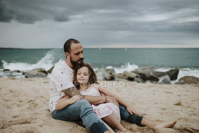 Pai abraçando filha enquanto sentado na praia — Fotografia de Stock