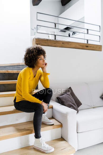 Mujer joven pensativa sentada en las escaleras en casa - foto de stock