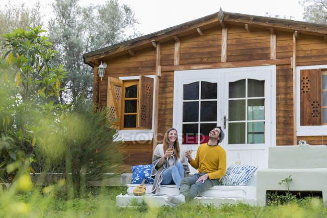 Casal alegre segurando vinhedos rindo enquanto sentado em passos de cabine de madeira — Fotografia de Stock