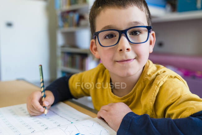 Carino ragazzo facendo i compiti mentre seduto alla scrivania durante coronavirus — Foto stock